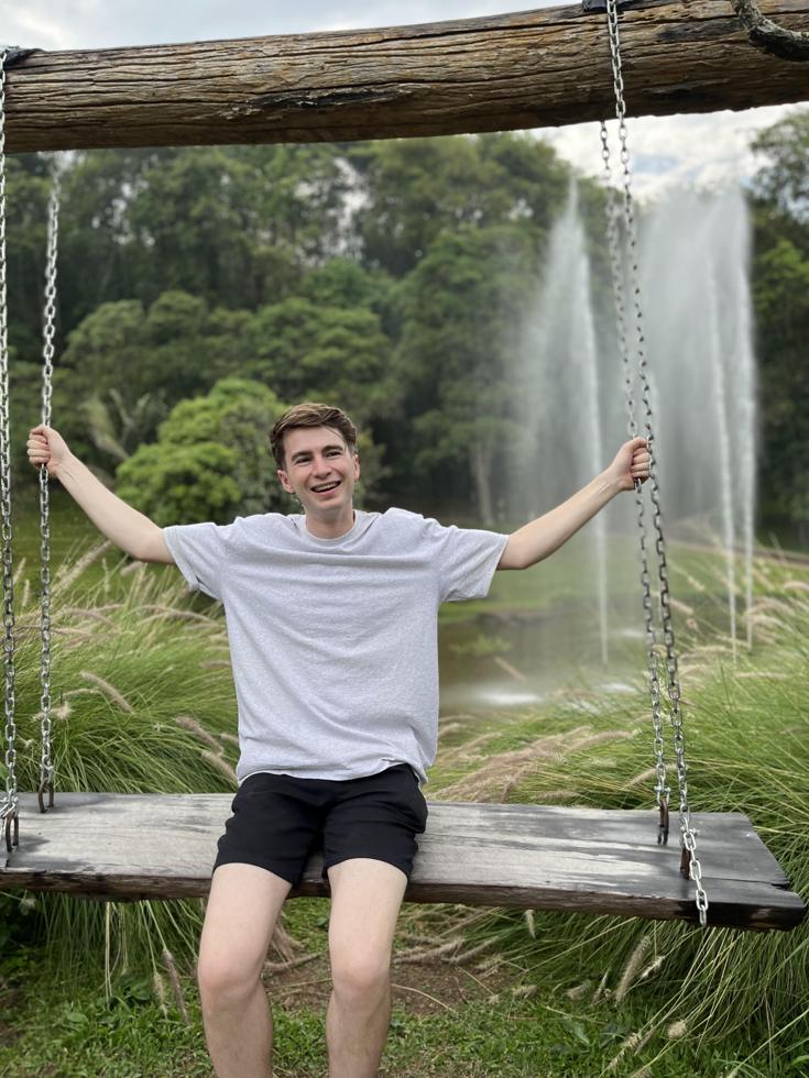 Stuart laughing on a wooden swing in front of fountains in northern Thailand